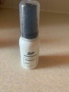 A short cylindrical black plastic bottle with a black plastic pump lid and a white label that has Boots Ingredients Vitamin C Serum written in bold black writing on it, on a white background.