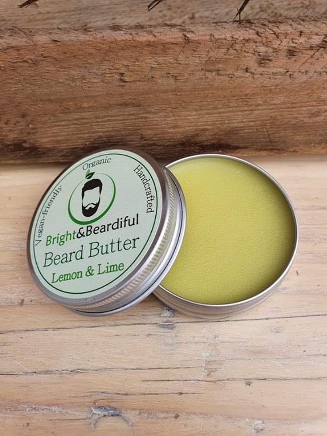 The Brightest Beard In The Box | Bright & Beardiful Lemon & Lime Beard Oil & Beard Butter Combo A short cylindrical open metallic Silver tin full of some creamy white beard butter with a white label that has Bright & Beardiful Lemon & Lime Beard Butter written in bold black writing and a picture of a person with a black beard on it, on a white background.