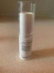 A short cylindrical white plastic tube with a white label that has Primark X Alex Steinherr Plump & Glow Facial In A Stick written in bold black writing on it, on a white background.