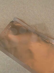 A small rectangular piece of clear card that has some small circular clear plastic stickers stuck on it on top of a large rectangular piece of silver foil, on a white background.