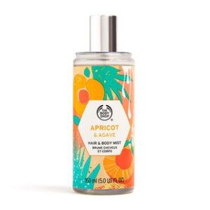 A tall cylindrical clear plastic bottle full of some clear liquid with a metallic silver spray lid and a clear label that has The Body Shop Apricot & Agave Hair & Body Mist written in bold black writing and some pictures of some golden pink apricots on it, on a white background.