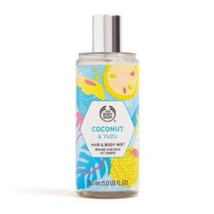 A tall cylindrical clear plastic bottle full of some clear liquid with a metallic silver spray lid and a clear label that has The Body Shop Coconut & Yuzu Hair & Body Mist written in bold black writing and some pictures of some bright yellow yuzus on it, on a white background.