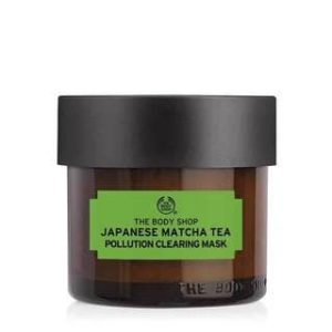 A short cylindrical clear glass Jar full of some creamy green liquid with a matte black plastic lid and a green label that has The Body Shop Japanese Matcha Tea Pollution Clearing Mask written in bold black writing on it, on a white background.