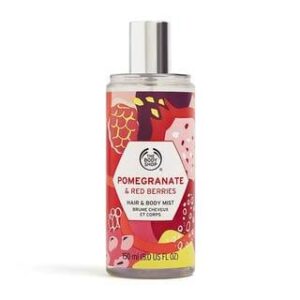A tall cylindrical clear plastic bottle full of some clear liquid with a metallic silver spray lid and a clear label that has The Body Shop Pomegranate & Red Berries Hair & Body Mist written in bold black writing and some pictures of some bright red berries on it, on a white background.