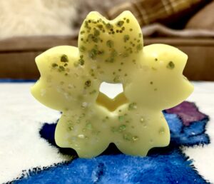 A large neon yellow flower shaped wax melt that's covered in some silver lustre, on a white background.