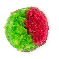 A small cylindrical clear glass jar full of some bright green and dark red lip scrub, on a white background.
