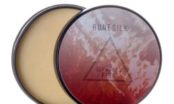 A short cylindrical silver open tin full of some golden yellow beard balm with a white and gradient red label that has Runesilk Elements Fire Beard Balm written in bold black writing and a picture of a red triangle on it, on a white background.
