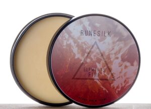 A short cylindrical silver open tin full of some golden yellow beard balm with a white and gradient red label that has Runesilk Elements Fire Beard Balm written in bold black writing and a picture of a red triangle on it, on a white background.