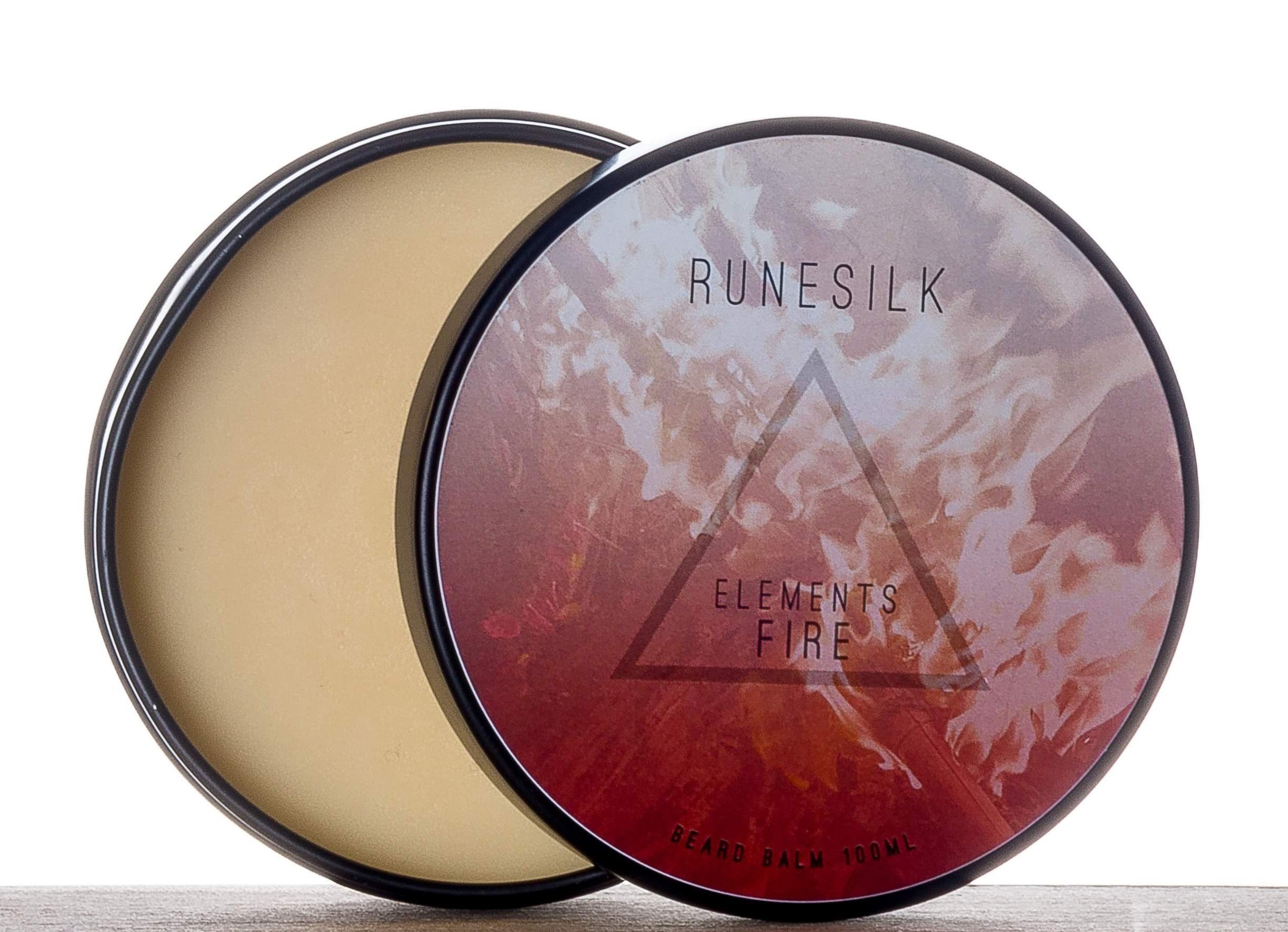 Careful! Don't Get Your Beard Too Close To The Fire | Runesilk Elements Fire Beard Balm & Beard Oil A short cylindrical silver open tin full of some golden yellow beard balm with a white and gradient red label that has Runesilk Elements Fire Beard Balm written in bold black writing and a picture of a red triangle on it, on a white background.