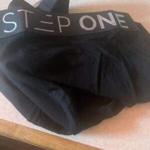 A large pair of black trunks that has Step One written in bold white writing on them, on a white background.