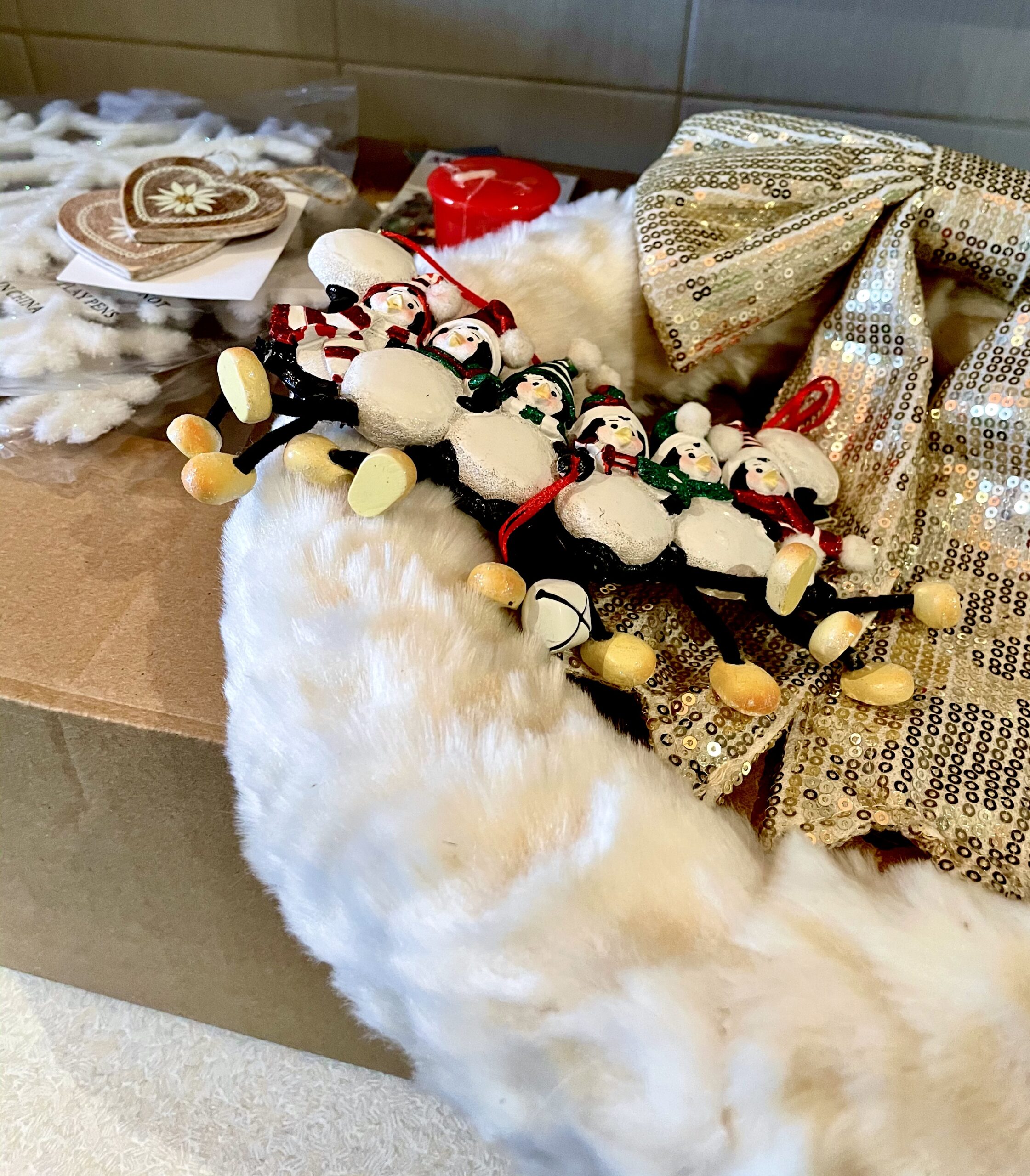It's A Christmas Mystery! | Christmas Shop Holt £20 Mystery Box | Gifted A collection of Christmas Decorations including some large white furry Snowflakes, a white circular furry Christmas Wreath with a Silver ribbon around it, a small rectangular wooden plaque that has some bells attached to the bottom of it, and some small Red and White wooden hearts, on a white background.