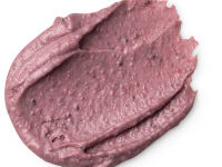 A small circular puddle of light purple face & body mask that has some pieces of dark brown aduki beans running through it, on a white background.
