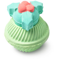 A large bright green spherical shaped bath bomb that has a holly and berry shaped bath bomb stopper on top of it, on a white background.