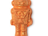 A small bright orange clockwork man shaped bath bomb that has some gold lustre on top of it, on a white background.