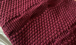 A large wine red folded up knitted scarf, on a white background.