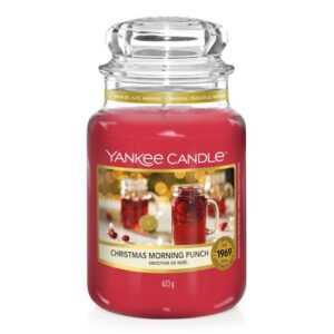 A tall cylindrical jar full of some dark red wax with a label that has Yankee Candle written in white writing, Christmas morning punch written in black writing, and a picture of a glass tumbler full of some dark red liquid surrounded by some out of focus fairy lights on it, on a white background.