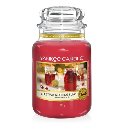 The Most Magical Scented Time Of The Year | Yankee Candle Magical Christmas Morning Collection A tall cylindrical jar full of some dark red wax with a label that has Yankee Candle written in white writing, Christmas morning punch written in black writing, and a picture of a glass tumbler full of some dark red liquid surrounded by some out of focus fairy lights on it, on a white background.