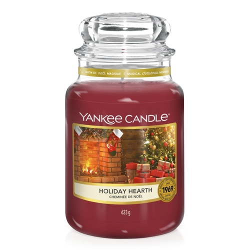 Sparkle Sparkle!| Yankee Candle Holiday Sparkle Collection A tall cylindrical Jar full of some dark red wax with a label that has Yankee Candle written in white writing, holiday hearth written in black writing, and a picture of a large dark green Christmas Tree covered in some fairy lights next to a large rectangular red brick fireplace that has a fire burning in it and some Christmas Stockings hung above it on it, on a white background.