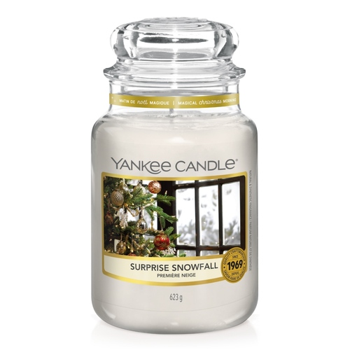 What I Thought of the Yankee Candle Advent House 2014 A tall cylindrical Jar full of some creamy white wax with a label that has Yankee Candle written in white writing, Surprise Snowfall written in black writing, and a picture of a large dark green Christmas Tree covered in some fairy lights next to a large rectangular window that's covered in snow on it, on a white background.