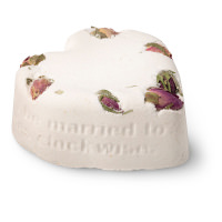 A large bright white heart shaped bath bomb that has seven dark red rosebuds embedded in it, on a white background.
