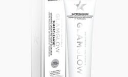 A tall thin conical white Plastic Tube with a silver Plastic Lid that has GlamGlow SuperCleanse™ Cream To Foam Cleanser written in bold black writing on it next to a tall rectangular white cardboard box that has GlamGlow SuperCleanse™ Cream To Foam Cleanser written in bold black writing and a picture of a silver star on it, on a white background.