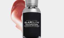 A tall thin cylindrical silver plastic Bottle with a silver pump lid with a black label that has GlamGlow YouthPotion™ Rejuvenating Peptide Serum written in bold white writing on it, on a white background