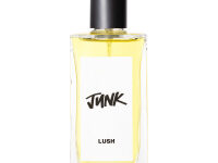A large rectangular glass perfume bottle full of some translucent purple liquid with a black metallic lid and a white label that has Lush Junk Perfume written in bold black writing on it, on a white background.