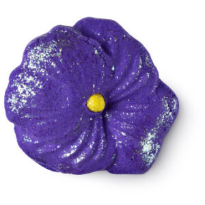 A large bright sparkly purple flower shaped bubble bar that has a bright yellow circle in the centre of it and a cut in the middle of it that’s filled with some bright white fondant icing, on a white background.