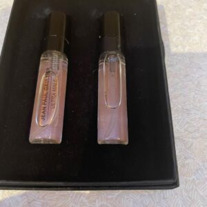 Two short cylindrical grey plastic glass Bottles with matte black plastic lids inside a small rectangular black cardboard box, on a white background.