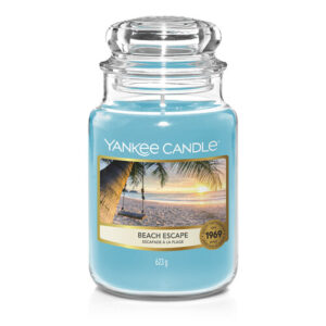 A tall cylindrical Jar full of some light blue Wax with a label that has Yankee Candle written in white writing, Beach Escape written in black writing, and a picture of a sandy beach on it, on a white background.