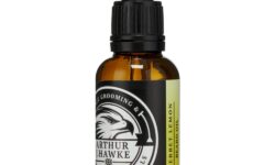A short cylindrical brown glass bottle with a black rubber pipette lid and a white label that has Arthur J Hawke Lemon Sherbet Beard Oil written in bold white writing and a picture of a black and white hawk on it, on a white background.