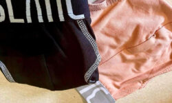 A pair of folded up peach briefs with a peach waistband that has Blanc Menswear written in bold black writing on it next to a pair of folded up black briefs that has Blanc Menswear written in bold blue writing on it, on a white background.