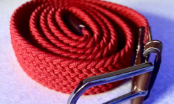 A bright red rolled up men's elastic belt with a shiny silver buckle, on a white background.