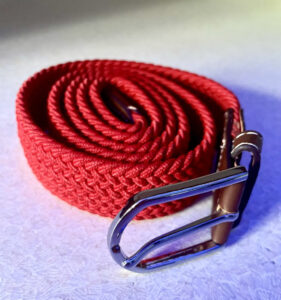 A bright red rolled up men's elastic belt with a shiny silver buckle, on a white background.