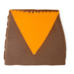 A large dark brown trapezium shaped block of soap that has a bright orange triangle embedded on the side of it, on a white background.