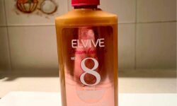 A tall rounded rectangular clear plastic bottle full of some clear liquid with a pink plastic nozzle lid that has L’Oreal Paris Elvive Dream Lengths Wonder Water written in bold white writing on it, on a white background.