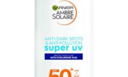 A short rectangular white plastic bottle with a white plastic lid that has Garnier Ambre Solaire written in bold black writing, Super UV written in light blue writing, Face Fluid SPF50+ written in bold gold writing, and a picture of a dark blue stripe on it, on a white background.
