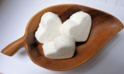 A small bright white heart shaped bath bomb that has some pieces of epsom salt embedded in it, on a white background.
