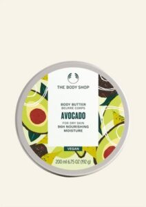 A short cylindrical light green plastic tub with a silver aluminium Lid that has The Body Shop Avocado Body Butter written in dark green writing and some pictures of some large bright green avocados on it, on a white background.