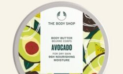 A short cylindrical light green plastic tub with a silver aluminium Lid that has The Body Shop Avocado Body Butter written in dark green writing and some pictures of some large bright green avocados on it, on a white background.
