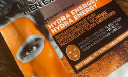 A tall rectangular silver plastic pouch that has L’Oreal Paris Men Expert Hydra Energetic Tissue Mask written in bold black writing and a picture of a mans face that's wearing a bright orange face mask on it, on a white background.