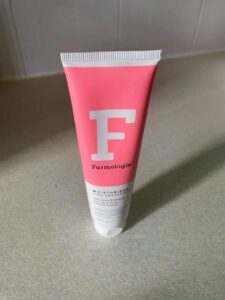 A tall conical white plastic tube that has Farmologie Pink Grapefruit Moisturiser written in bold black writing, a picture of a large white letter f, and a pink stripe on it, on a white background.