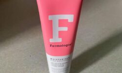 A tall conical white plastic tube that has Farmologie Pink Grapefruit Moisturiser written in bold black writing, a picture of a large white letter f, and a pink stripe on it, on a white background.