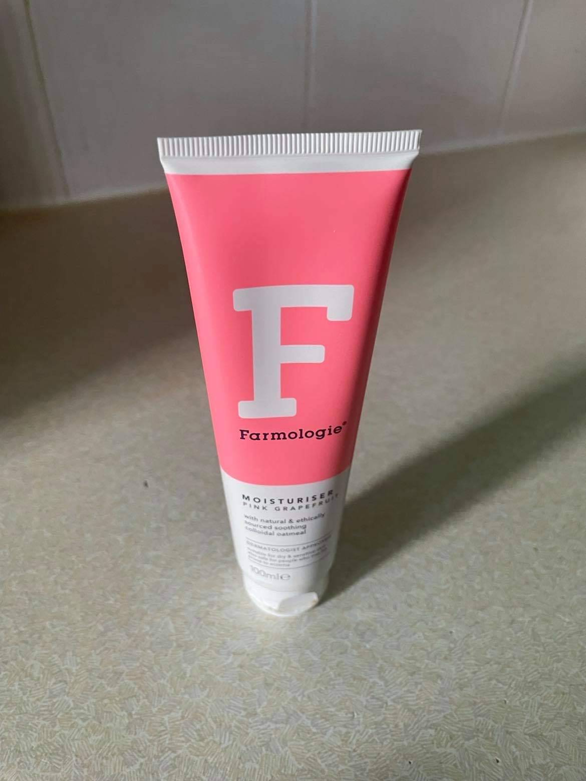 The Soothing Technology Of Pink Grapefruit | Farmologie Pink Grapefruit Moisturiser A tall conical white plastic tube that has Farmologie Pink Grapefruit Moisturiser written in bold black writing, a picture of a large white letter f, and a pink stripe on it, on a white background.