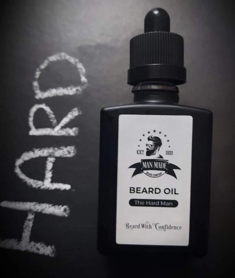 Five Of My Favourite Products From 2021 A short rectangular brown glass Bottle with a black rubber pipette lid and a white label that has Man Made Beard Company The Hard Man Beard Oil written in bold black writing and a picture of a man with a black beard on it, on a white background.