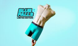 A tall white mannequin wearing a pair of teal blue boxer briefs with a black waistband that has Step One written in bold blue writing on it, on a blue background.