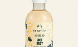 A tall cylindrical clear plastic bottle full of some pale yellow liquid with a white plastic lid and a pale yellow label that has The Body Shop Cool Daisy Shower Gel written in dark green writing and a picture of some pale yellow Daisies on it, on a white background.