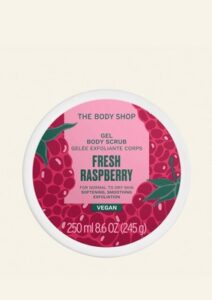 A short cylindrical white plastic tub with a white plastic lid and a bright pink label that has The Body Shop Fresh Raspberry Gel Body Scrub written in dark green writing and a picture of some dark red raspberries on it, on a white background.