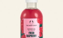 A tall cylindrical clear plastic bottle full of some dark red liquid with a white plastic lid and a bright pink label that has The Body Shop Fresh Raspberry Shower Gel written in dark green writing and a picture of some dark red raspberries on it, on a white background.