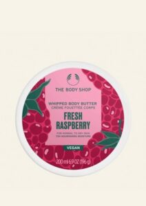 A short cylindrical white plastic tub with a white plastic lid and a bright pink label that has The Body Shop Fresh Raspberry Whipped Body Butter written in dark green writing and a picture of some dark red raspberries on it, on a white background.